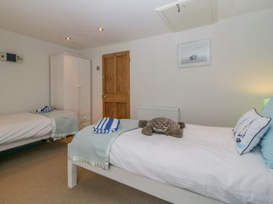 A bedroom with two single beds one with a stuffed turtle and a pillow a white wardrobe and a wooden door at Curlews Cottage in Looe