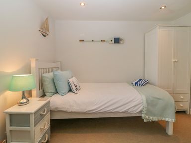 A bedroom with a single bed with pillows and a blanket a nightstand with a lamp and a wardrobe at Curlews Cottage in Looe