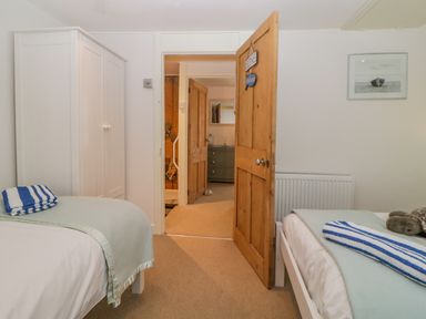 A bedroom with two single beds a white wardrobe and an open wooden door at Curlews Cottage in Looe