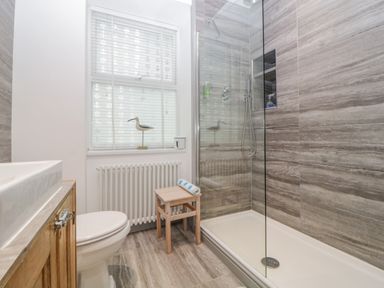 A bathroom with a shower area a toilet a sink a wooden stool and a window at Curlews Cottage in Looe