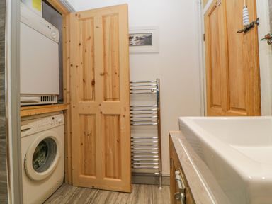 A laundry area with a washing machine and dryer behind wooden doors next to a sink and towel rack at Curlews Cottage in Looe