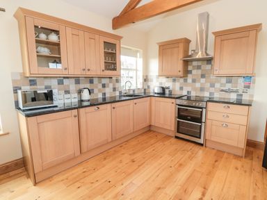 A kitchen with wooden cabinets tiled backsplash and appliances at Bank Top Cottage in Embleton