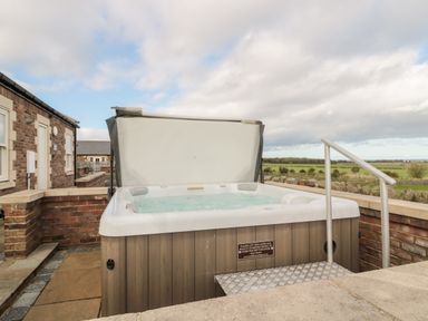 An outdoor hot tub with a raised cover on a stone patio next to a brick building with fields in the background at Bank Top Cottage in Embleton