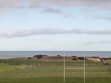 A rugby field with goalposts and a wooden fence overlooking fields and the sea at Bank Top Cottage in Embleton
