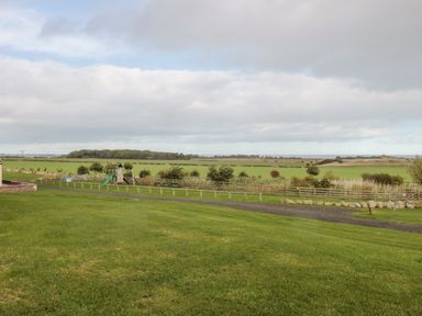 A grassy field with a playset slide and wooden fence in a rural area at Bank Top Cottage in Embleton