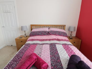 A bedroom with a bed with patterned bedding and two bedside tables with lamps at 1 Beachtop Court in Tenby