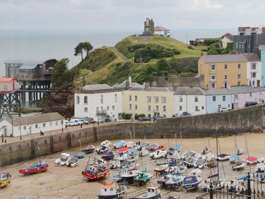 A harbor with boats docked on the sand near a row of buildings and a grassy hill with a monument at 1 Beachtop Court in Tenby
