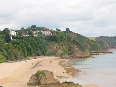 A sandy beach with a large rock and a white vehicle near the shoreline with cliffs and houses in the background at 1 Beachtop Court in Tenby