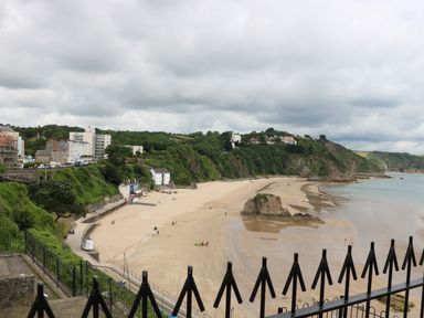 A sandy beach with rock formations people and buildings on a cliff at 1 Beachtop Court in Tenby