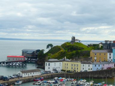 A harbor with boats docked near colorful buildings and a grassy hill with a monument at 1 Beachtop Court in Tenby