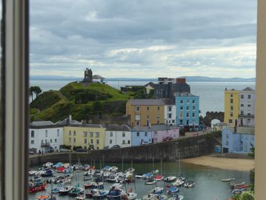 A harbor with boats docked near colorful buildings and a grassy hill with a monument and ocean view at 1 Beachtop Court Tenby