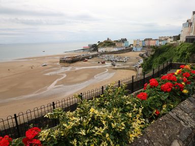 A beach with boats on sand near a harbor with colorful buildings and flowers in the foreground at 1 Beachtop Court in Tenby
