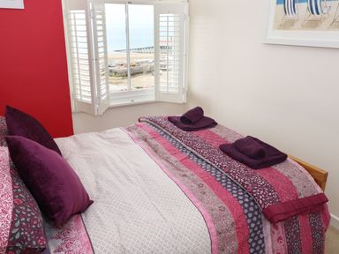 A bedroom with a patterned bedspread and purple pillows next to a window with white shutters overlooking a beach at 1 Beachtop Court Tenby