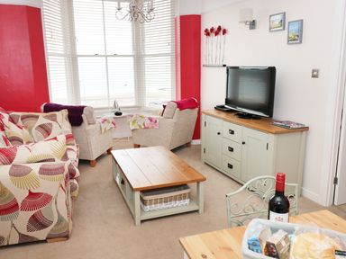 A living room with a patterned sofa two armchairs a wooden coffee table and a TV on a cabinet at 1 Beachtop Court in Tenby
