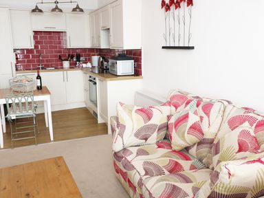 A kitchen and living area with white cabinets red tile backsplash patterned sofa wooden table and metal chairs at 1 Beachtop Court Tenby