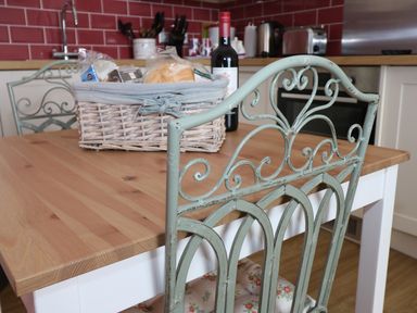 A kitchen table with a wicker basket containing groceries and a bottle of wine with a metal chair in the foreground at 1 Beachtop Court in Tenby