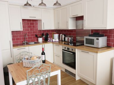 A kitchen with white cabinets red tiled backsplash and wooden countertops at 1 Beachtop Court in Tenby