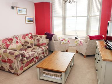 A living room with patterned sofa two armchairs wooden coffee table and TV unit at 1 Beachtop Court in Tenby