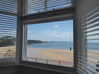 A view of a sandy beach and ocean through a window with white blinds at 1 Beachtop Court in Tenby