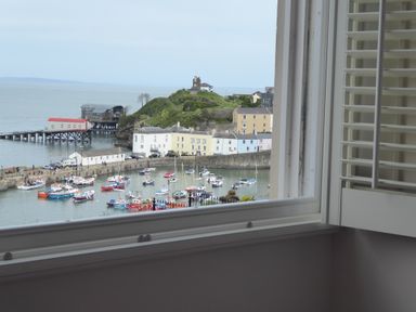 A view through a window showing a harbor with boats and houses near the water at 1 Beachtop Court in Tenby