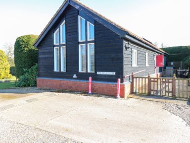 A black wooden chalet with large windows and a red brick base in a garden at Rookyard Cottage Holton near Halesworth