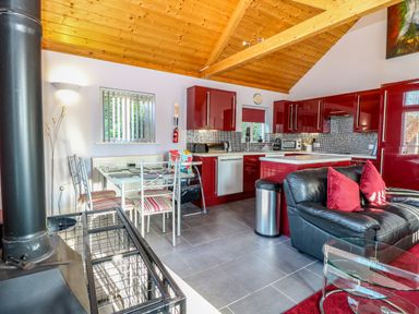 A kitchen and dining area with red cabinets and a black sofa with red pillows at Rookyard Cottage in Holton near Halesworth