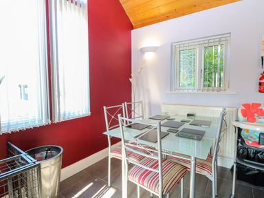 A dining area with a glass table and four metal chairs with striped cushions at Rookyard Cottage in Holton near Halesworth