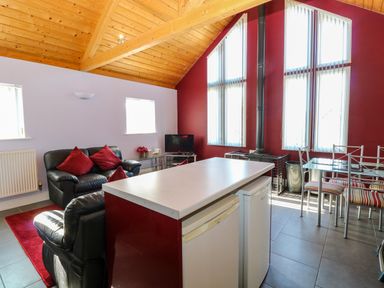 A living room with black leather sofas red cushions dining table and high ceiling with wood paneling at Rookyard Cottage in Holton near Halesworth