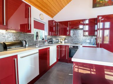 A kitchen with red cabinets white countertops a tiled backsplash and kitchen appliances at Rookyard Cottage in Holton near Halesworth
