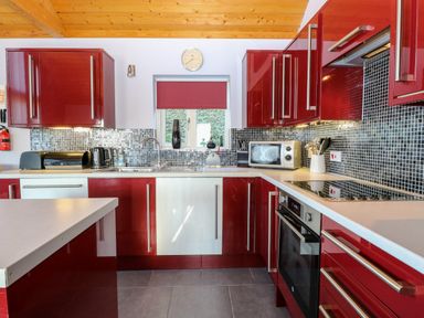 A kitchen with red and white cabinets a tiled backsplash and appliances at Rookyard Cottage in Holton near Halesworth