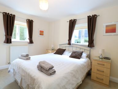 A bedroom with a double bed two bedside tables and windows with brown curtains at Rookyard Cottage in Holton near Halesworth