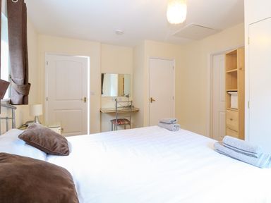 A bedroom with a bed with brown pillows folded towels on the bed a desk and chair two doors and a shelving unit at Rookyard Cottage in Holton near Halesworth