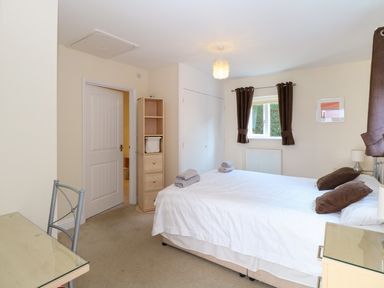 A bedroom with a double bed with brown pillows and towels a small shelving unit a desk with chair and a window with brown curtains at Rookyard Cottage in Holton near Halesworth