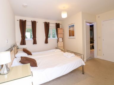 A bedroom with two single beds a bedside table and lamp and windows with brown curtains at Rookyard Cottage in Holton near Halesworth