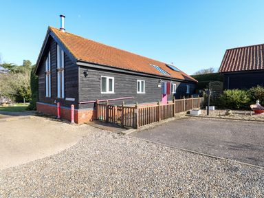 A black wooden building with a red tiled roof and small windows and a wooden fence at Rookyard Cottage in Holton near Halesworth