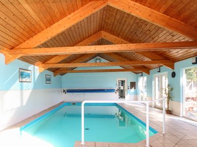 An indoor swimming pool with light blue walls wooden ceiling beams and tiled floor at Rookyard Cottage in Holton near Halesworth