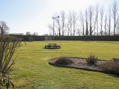 A large grassy garden with a picnic table play equipment and a covered seating area at Rookyard Cottage Holton near Halesworth