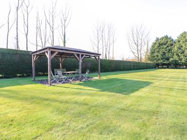 A wooden gazebo with chairs and a table on a grass lawn surrounded by trees at Rookyard Cottage in Holton near Halesworth