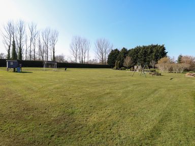 A large grassy field with a small playhouse a soccer goal and a swing set with picnic benches at Rookyard Cottage in Holton near Halesworth