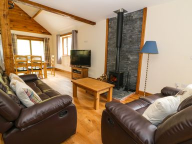 A living room with leather sofas a wooden coffee table a wood stove and a dining table at Ploony Hill Lodge in Bleddfa