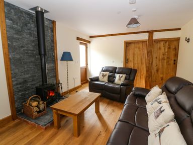 A living room with a wood burning stove two leather sofas a wooden coffee table and cushions at Ploony Hill Lodge in Bleddfa