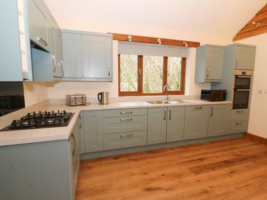 A kitchen with grey cabinets wooden floor and a window above the sink at Ploony Hill Lodge in Bleddfa