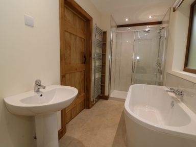 A bathroom with a pedestal sink wooden door bathtub walk in shower and towel rack at Ploony Hill Lodge in Bleddfa