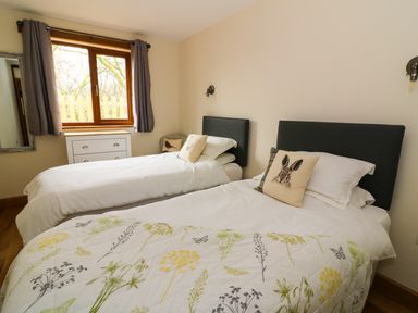 A bedroom with two single beds a window with curtains a chest of drawers and a mirror at Ploony Hill Lodge in Bleddfa