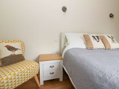 A bedroom with a bed with animal print pillows a wooden side table and a yellow patterned chair at Ploony Hill Lodge in Bleddfa
