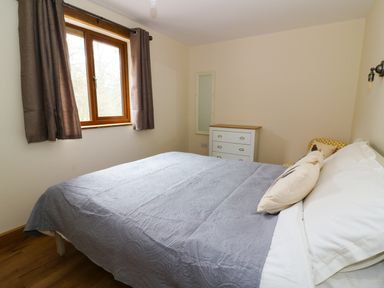A bedroom with a bed covered with gray quilt next to a window with brown curtains and a white chest of drawers at Ploony Hill Lodge in Bleddfa