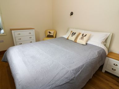 A bedroom with a bed covered with a gray quilt and animal print pillows a white dresser and a chair with a bird pillow at Ploony Hill Lodge in Bleddfa