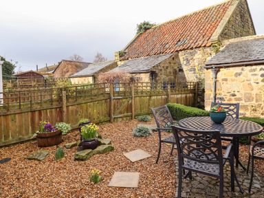A fenced garden with gravel ground and outdoor metal table with chairs at Jasmine Cottage in Lesbury near Alnmouth