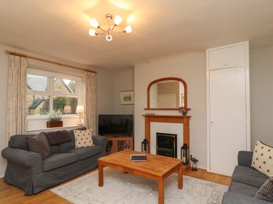 A living room with two sofas a wooden coffee table a fireplace a television and a window with curtains at Jasmine Cottage in Lesbury near Alnmouth