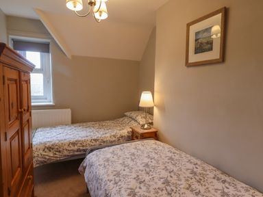 A bedroom with two single beds a wooden wardrobe a bedside table with a lamp and a framed picture on the wall at Jasmine Cottage in Lesbury near Alnmouth